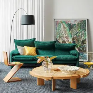 Green upholstered sofa with mustard cushions beside a round wood coffee table and arc lamp