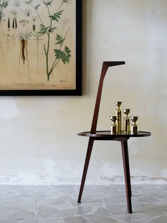 Wood side chair with angled backrest holding brass bottles beside a botanical print