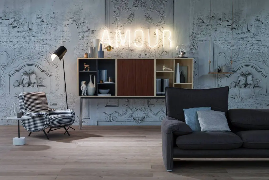 Living room with neon Amour sign, wall shelving unit, dark sofa and checked armchair