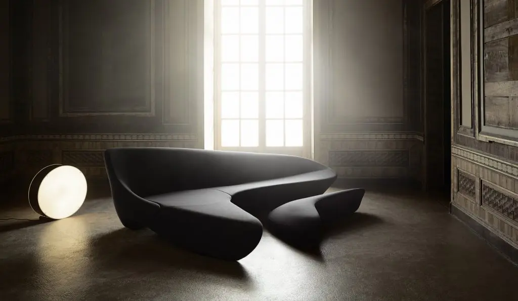 Sculptural black curved sofa lit by a glowing globe lamp in a shadowy paneled room