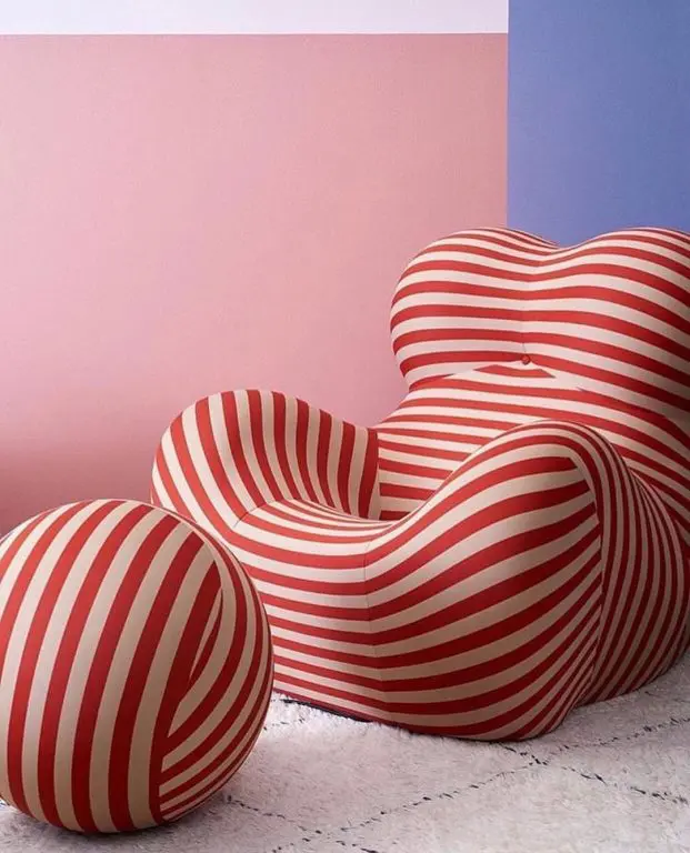 Red and cream striped armchair with a matching round pouf against a pink and blue wall