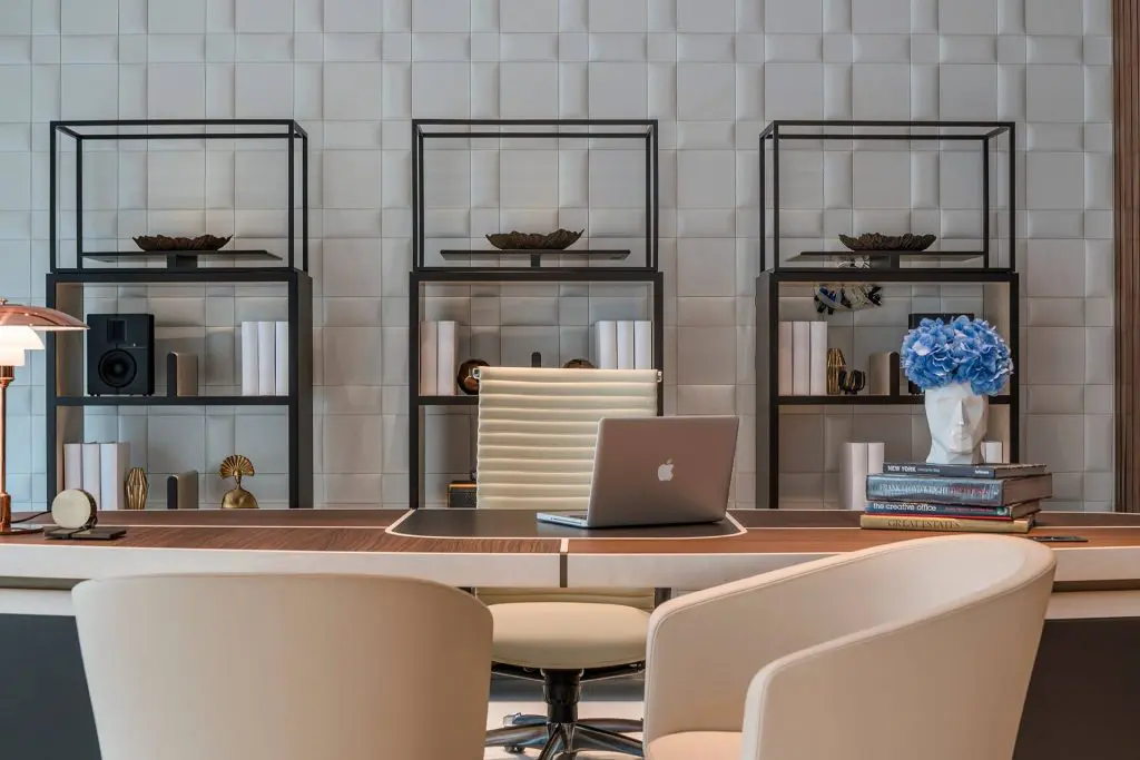 Office space with three black-framed shelving units, a long desk and cream chairs