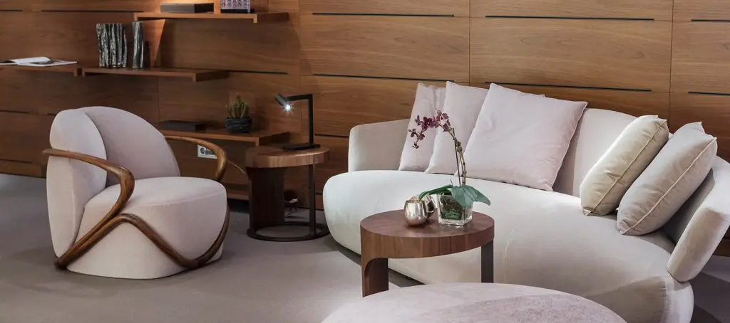 Curved wood-framed armchair beside a round sofa and wood coffee table on a wood-panelled wall