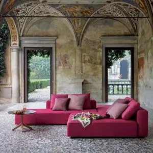 Magenta sectional sofa under a frescoed loggia ceiling opening to a garden courtyard