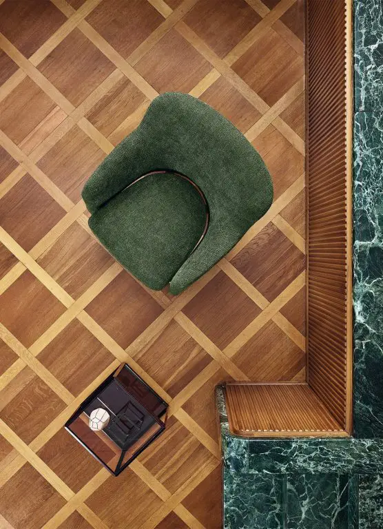 Overhead view of a green upholstered swivel chair on a herringbone wood and marble floor