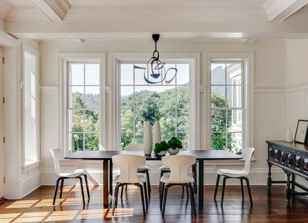 Dining room with black table, white shell-back chairs and a wire pendant chandelier