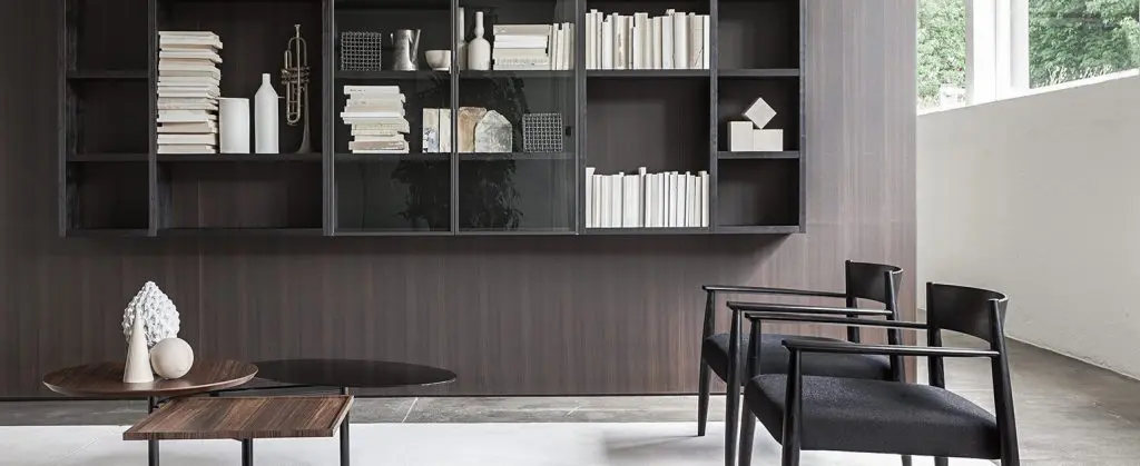 Wood-panelled reading nook with dark shelving, round side tables and leather armchairs