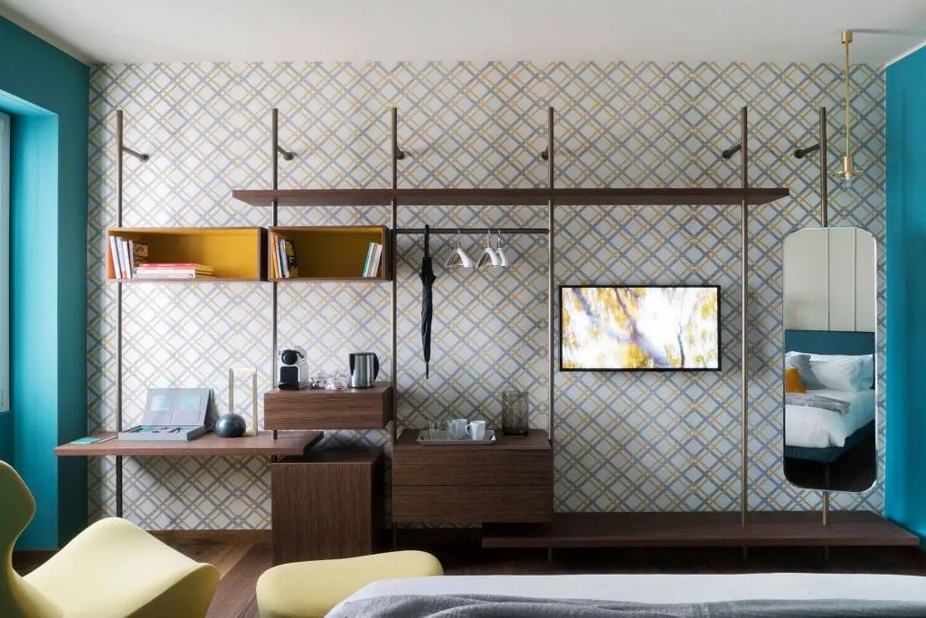 Hotel room with diamond-patterned wallpaper, open wardrobe rail and wall-mounted TV