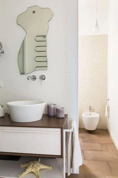 Bathroom with a sculptural body-shaped mirror, vessel sink and wood vanity cabinet