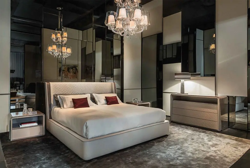 Bentley Home bedroom with a quilted taupe headboard bed, red cushions, mirrored panels and a crystal chandelier
