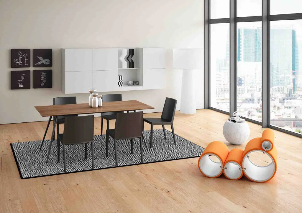Dining table with dark chairs, a white wall unit and an orange sculptural sofa by floor-to-ceiling windows