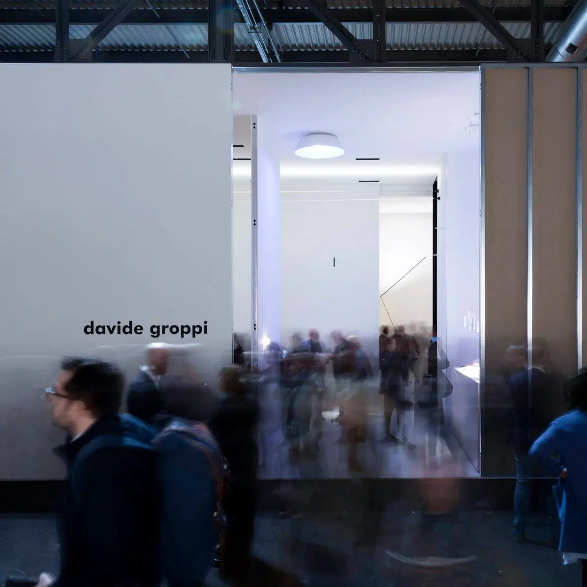 white structure with black text 'davide groppi' at euroluce 2019 with people moving and walking through the space