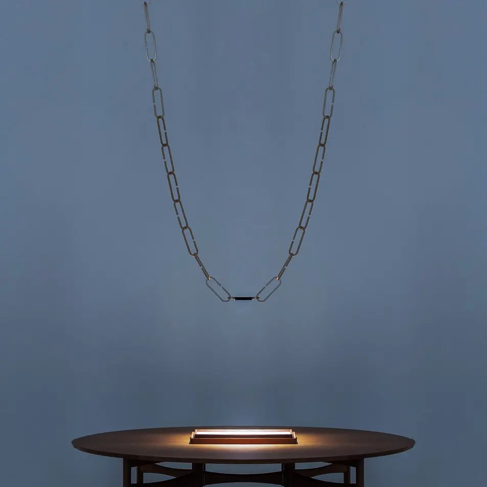 a large chain with a light at the end of the chain dangles above a small table with a grey wall background