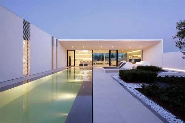 modern villa with an infinity pool and illuminated glass facade at dusk