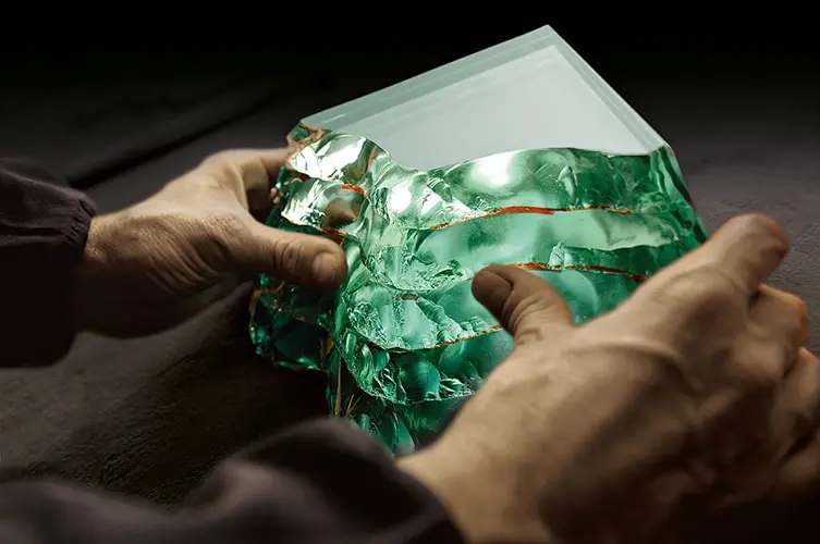Hands shaping a block of green molten glass in a workshop