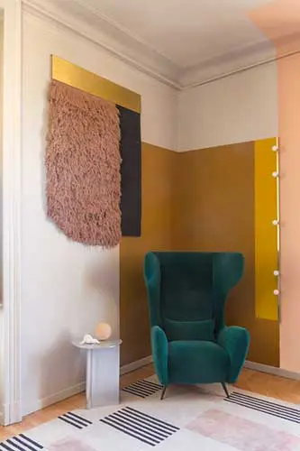 green wingback armchair beside a woven wall hanging in a two-tone painted room