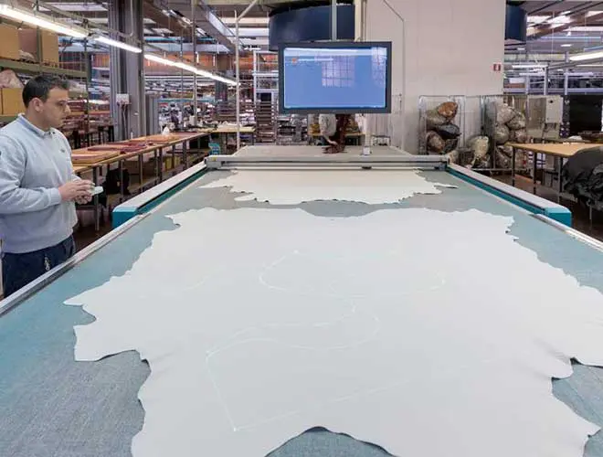 factory worker cutting a leather hide on a large cutting table