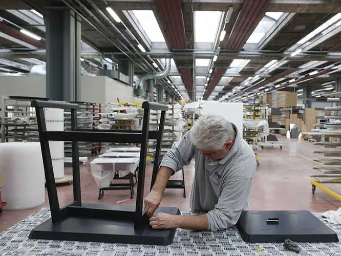 Worker assembling a black wood chair frame in a furniture factory