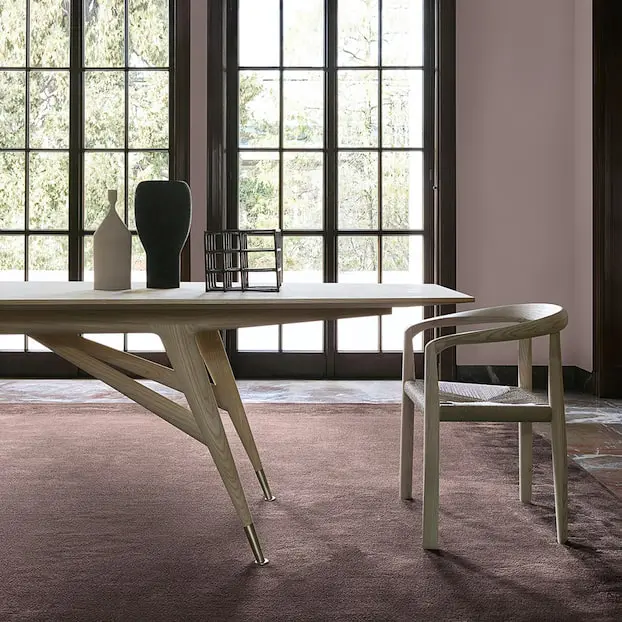 Angular wood dining table and chair by tall paned windows overlooking greenery