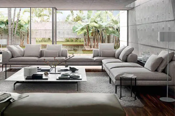 Modern grey sectional sofas in a living room facing a garden with palm trees