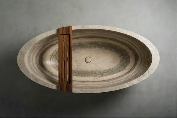 Overhead view of an oval carved stone bathtub with a wood accent panel