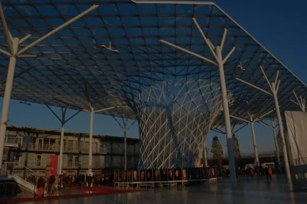 Glass canopy pavilion with tree-like steel supports at a Milan design event