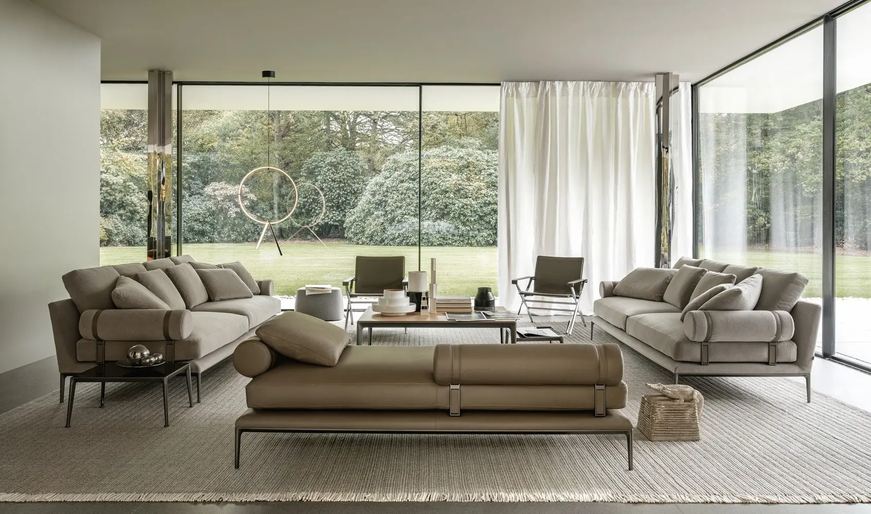 Beige sofas and a daybed in a glass-walled living room facing a garden