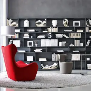 Red sculptural armchair and grey chair in front of a dark bookshelf filled with books and decor