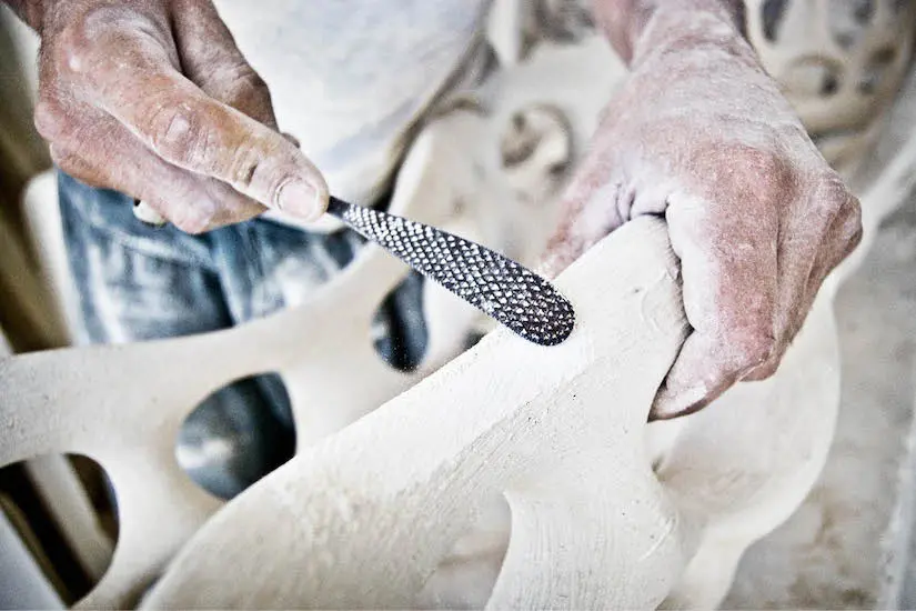 Craftsman's hands shaping a white stone sculpture with a rasp