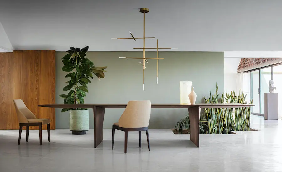 Dining area with a wooden table, beige chair and a linear brass pendant light against a sage green wall