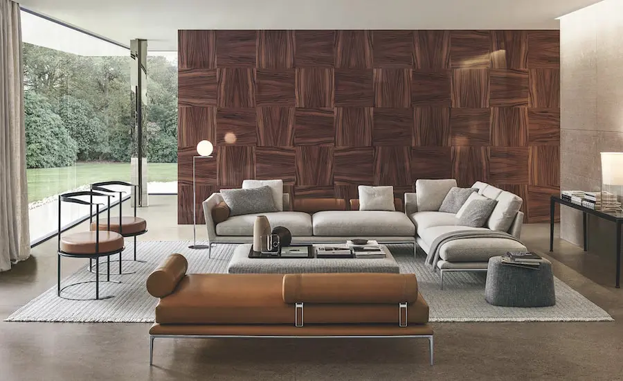 Living room with a light grey sofa, cognac leather bench and a wood parquet-patterned feature wall