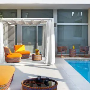 Poolside terrace with orange woven lounge chairs, a white pergola and round rattan side tables