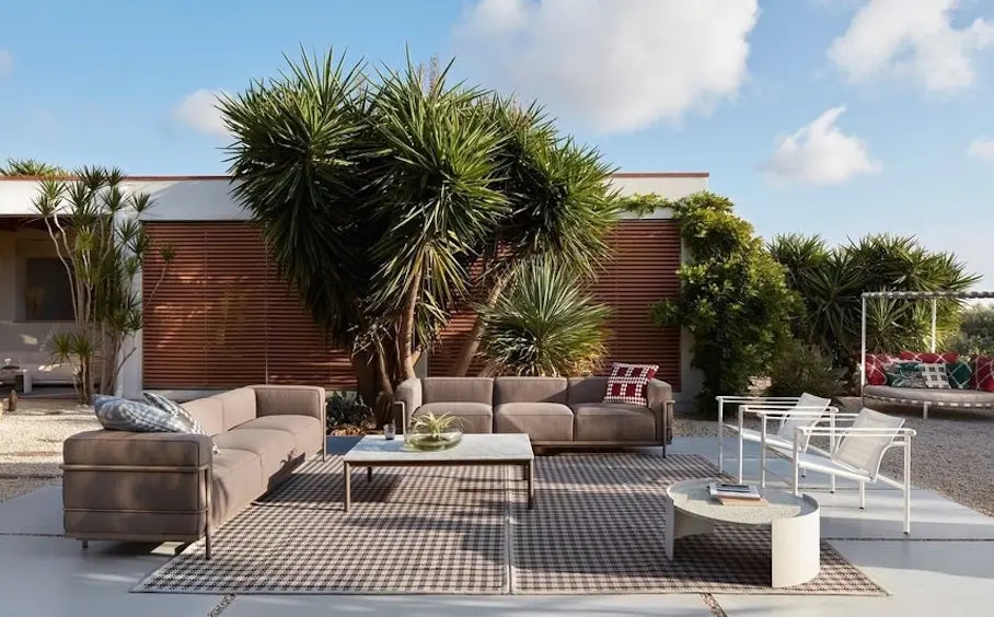 Terrace with a taupe modular sofa, marble coffee table and side table beneath a large yucca against wood slat cladding
