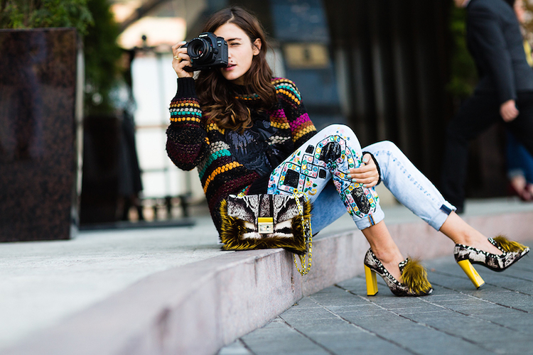 woman with brown hair sitting on street curb looking through a camera