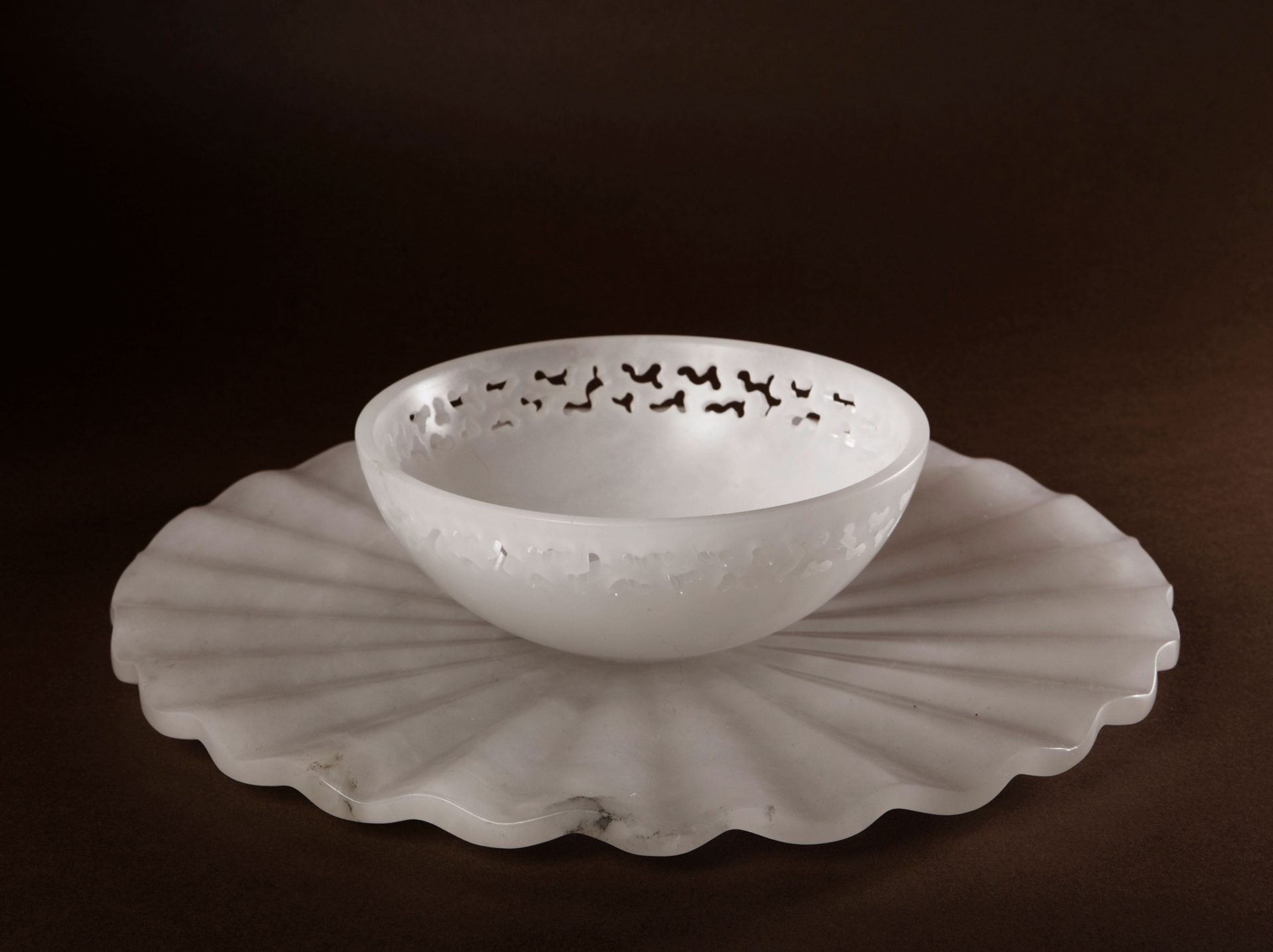 a white ceramic bowl atop a white ceramic plate with waves with a black background