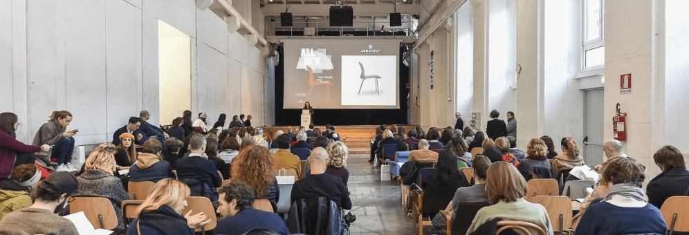 an audience in an indoor venue with a large screen with an image of a chair