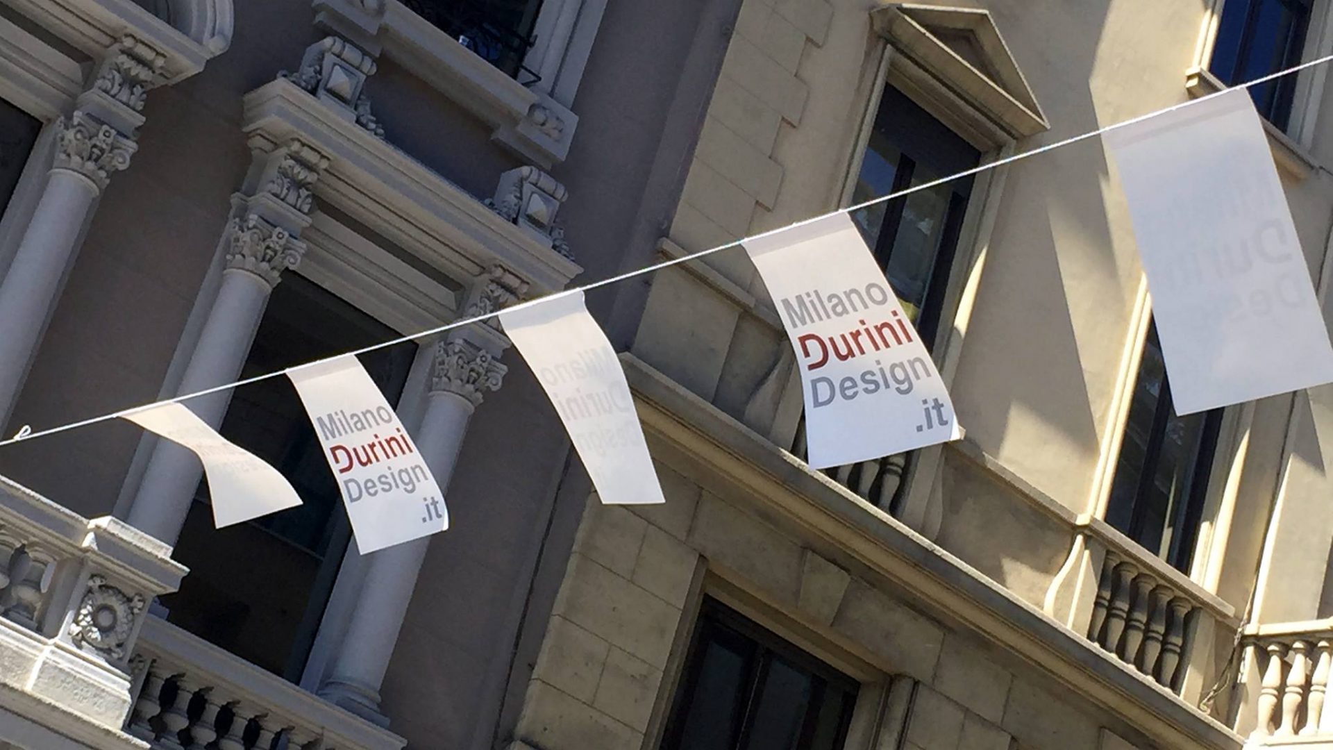 white flags with red text and historic buildings in milan in the background