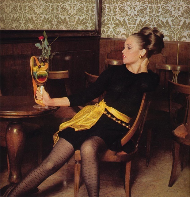 a woman with a hairdo in a black dress having a drink at a table