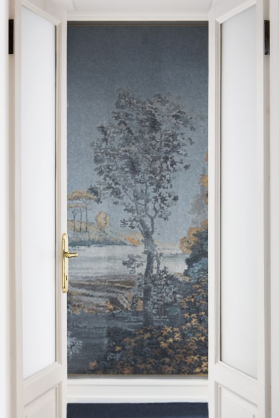 white doorway opening to a mosaic wall made of tiny glass squares of a tree and water scene