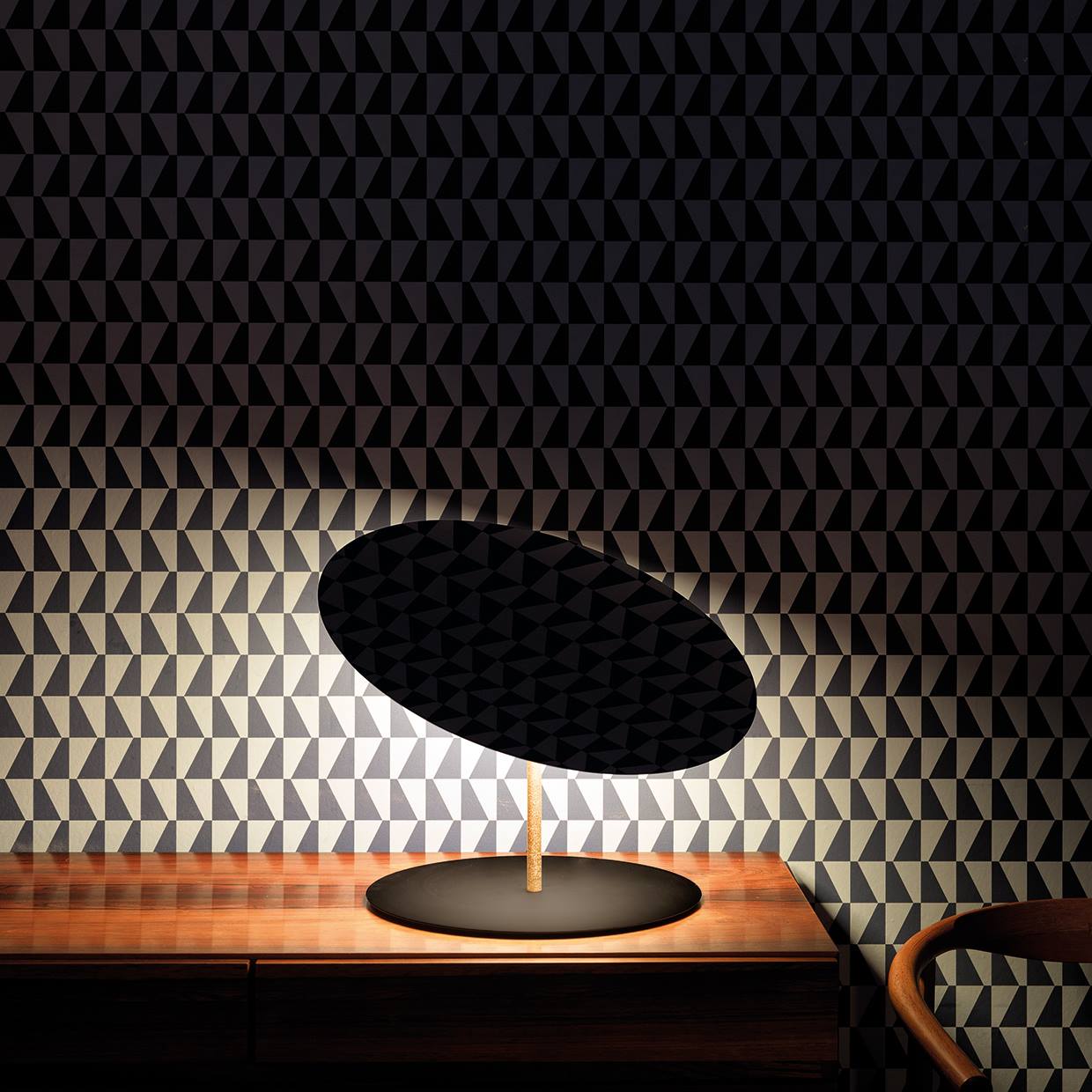 small round table lamp on a wooden desk with a patterned wallpaper with black and white geometric shapes