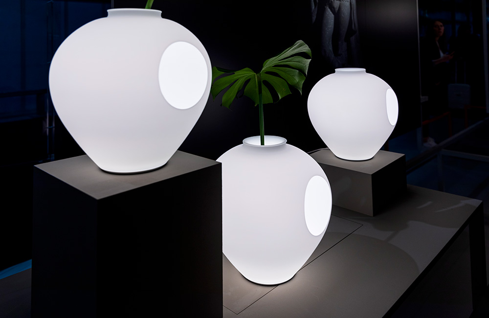 three large white lamps with round circles displayed on black platforms at Euroluce