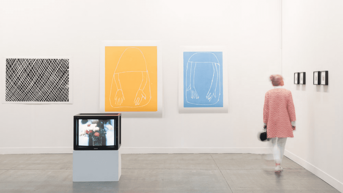 yellow and blue framed artworks on the wall with a woman in a pink coat walking by